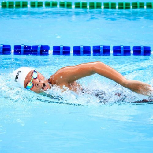 A swimmer energetically performs a freestyle stroke in a clear outdoor swimming pool, showcasing competitive spirit.